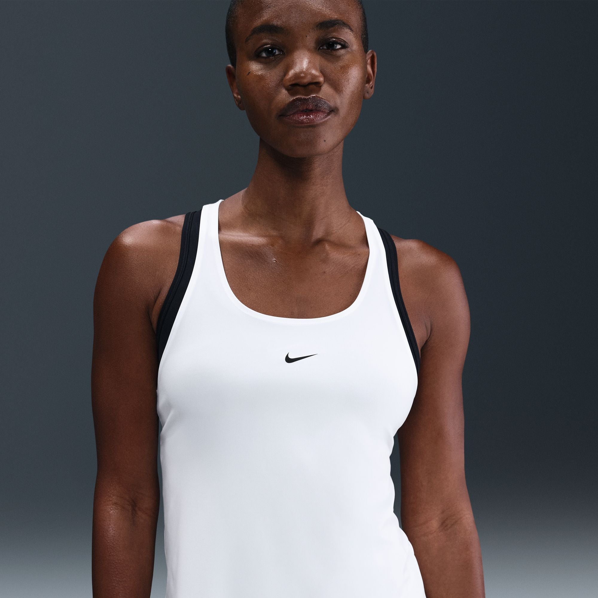 Woman wearing a white tank top with a black Nike logo on a gray background