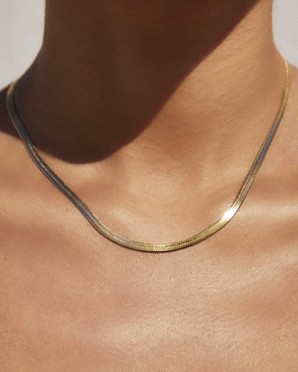 Gold necklace on a person's neck with a neutral background