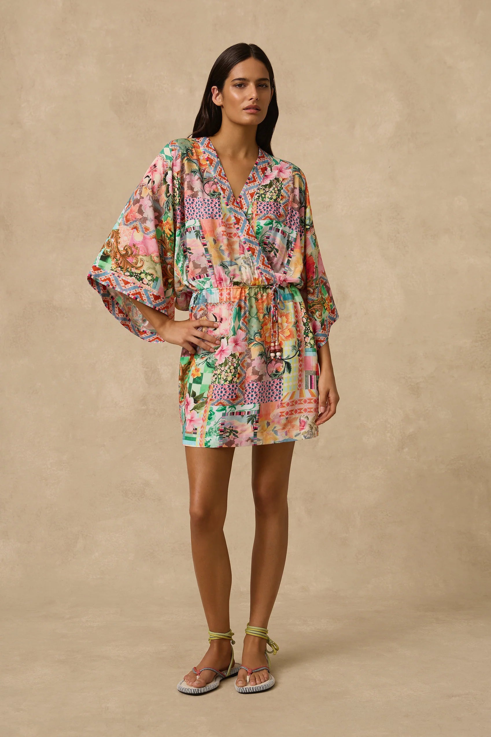 The Simi Kimono Mini Dress features a wrap front and wide kimono sleeve with border print band edge. Self Drawcord waist tie with coloured bead detail and straight skirt. Straight skirt.