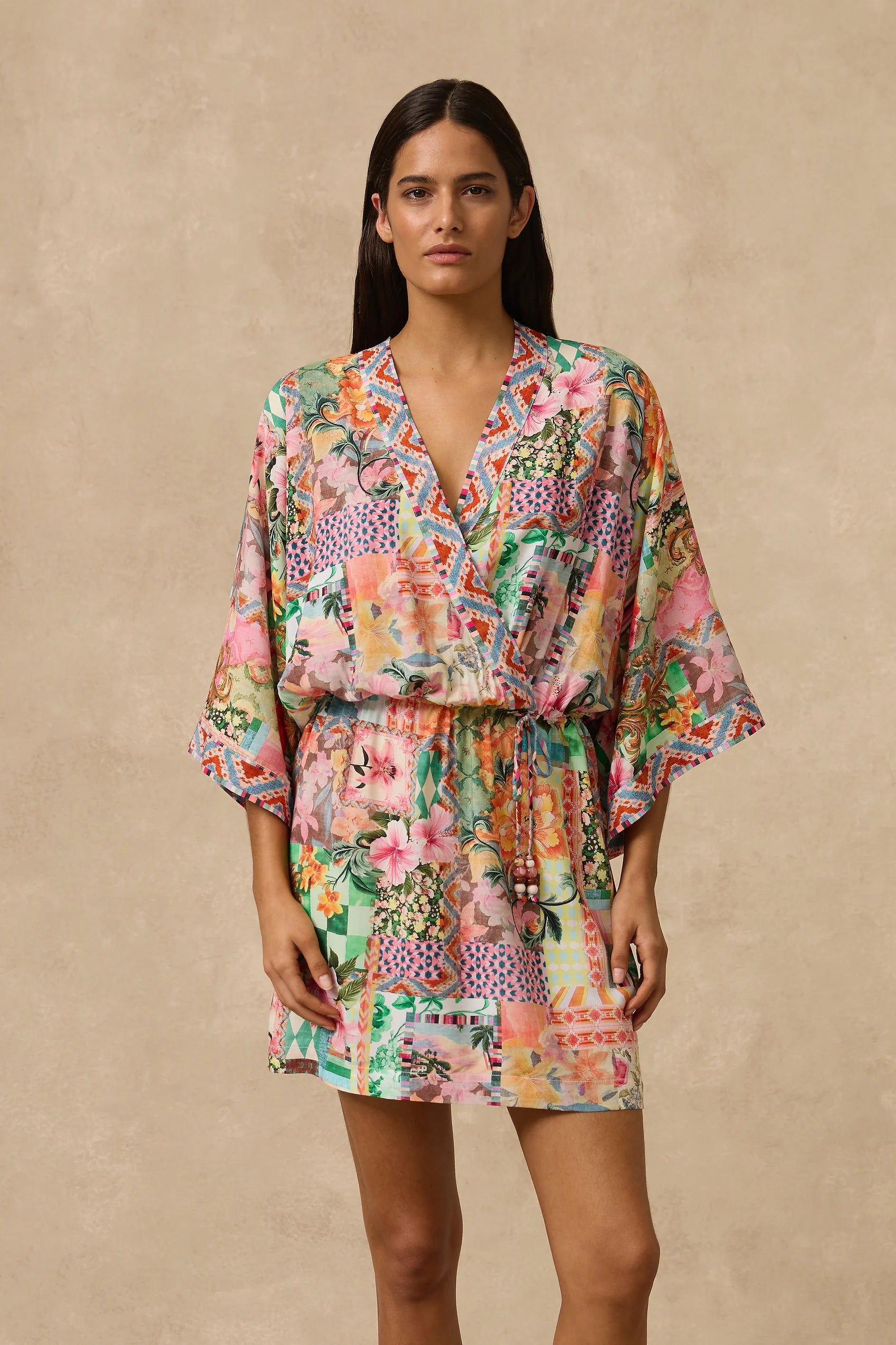 The Simi Kimono Mini Dress features a wrap front and wide kimono sleeve with border print band edge. Self Drawcord waist tie with coloured bead detail and straight skirt. Straight skirt.