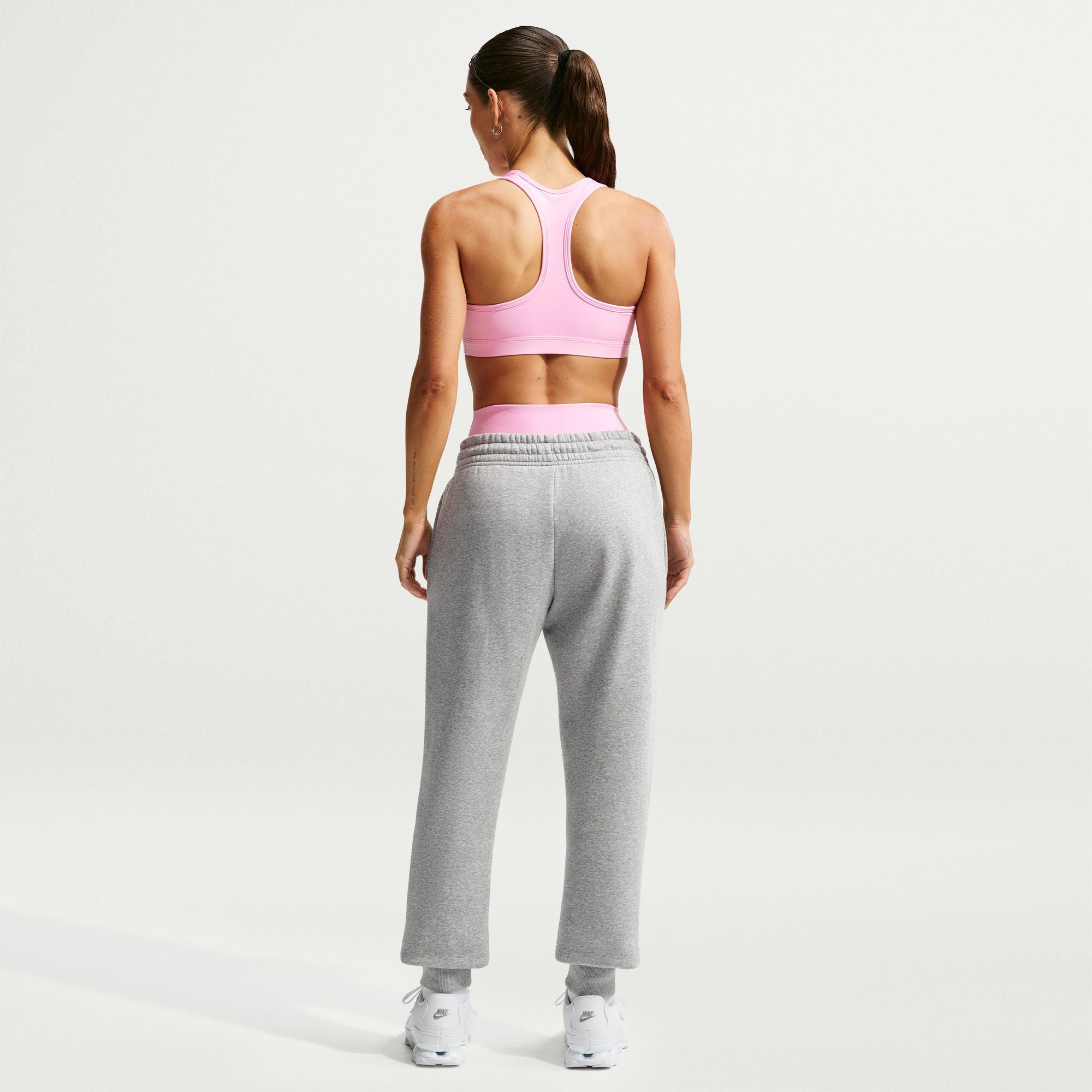 Woman wearing a pink sports bra and gray sweatpants on a light gray background