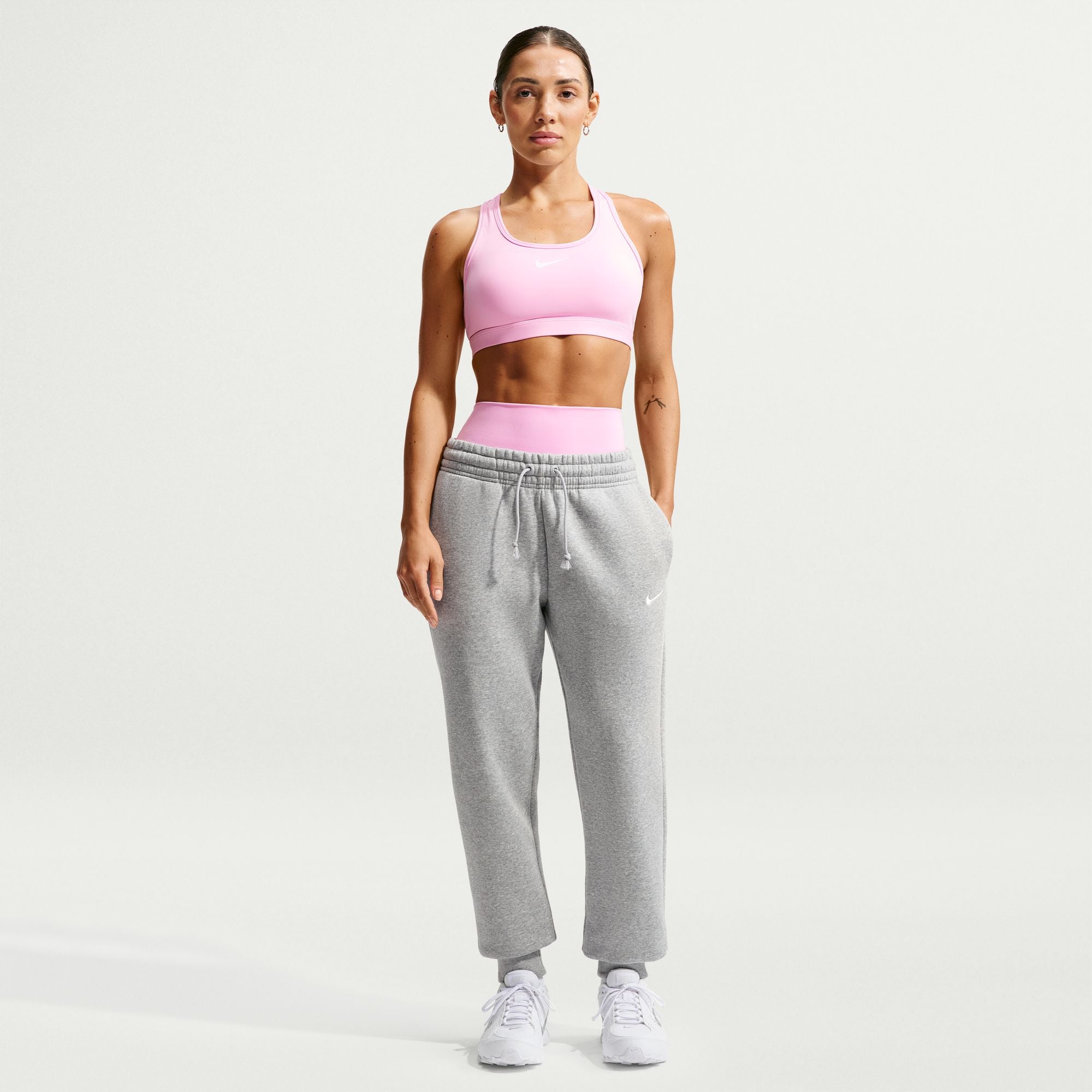 Woman wearing a pink sports bra and gray sweatpants on a white background