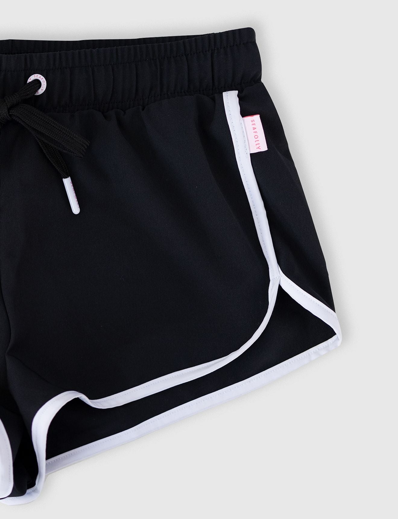 Seafolly Girls Essentials Boardshort in Black features an elasticated waistband, draw cord, scallop hemline, contrast piping.