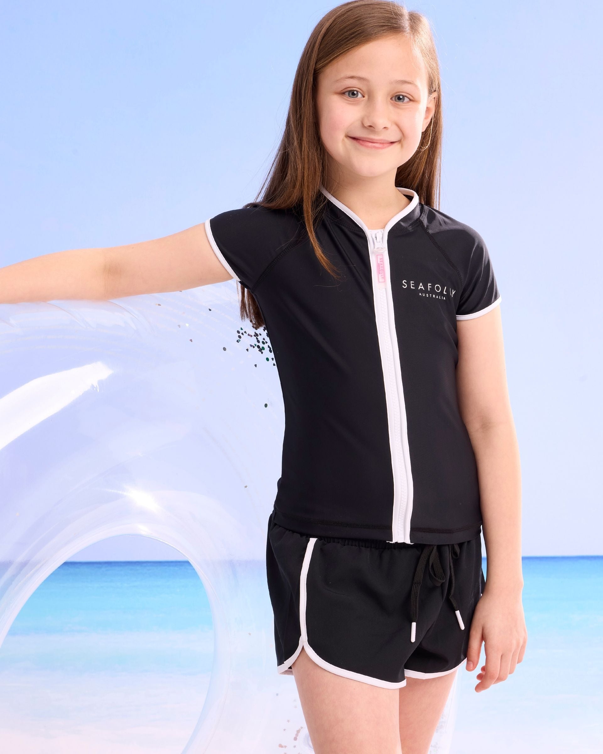Seafolly Girls Essentials Boardshort in Black features an elasticated waistband, draw cord, scallop hemline, contrast piping.