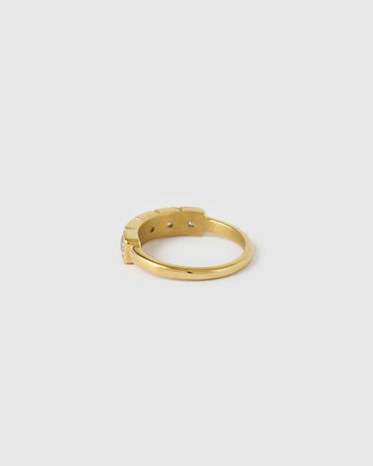 A gold-plated metal ring with a textured, geometric segmented band, shown from a side profile view on a light gray background.