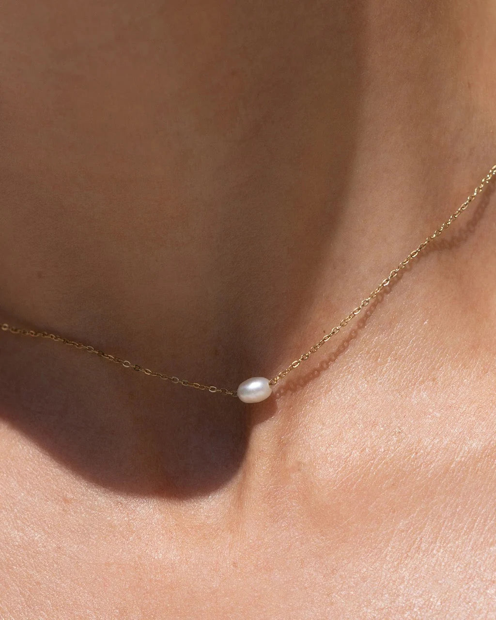 Gold necklace with a single pearl pendant on a person's neck