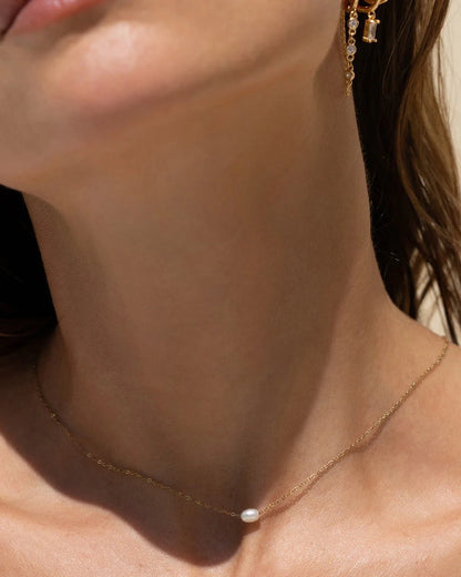 Close-up of a model's neck and lower face wearing a delicate gold chain necklace with a single small white pearl pendant,
