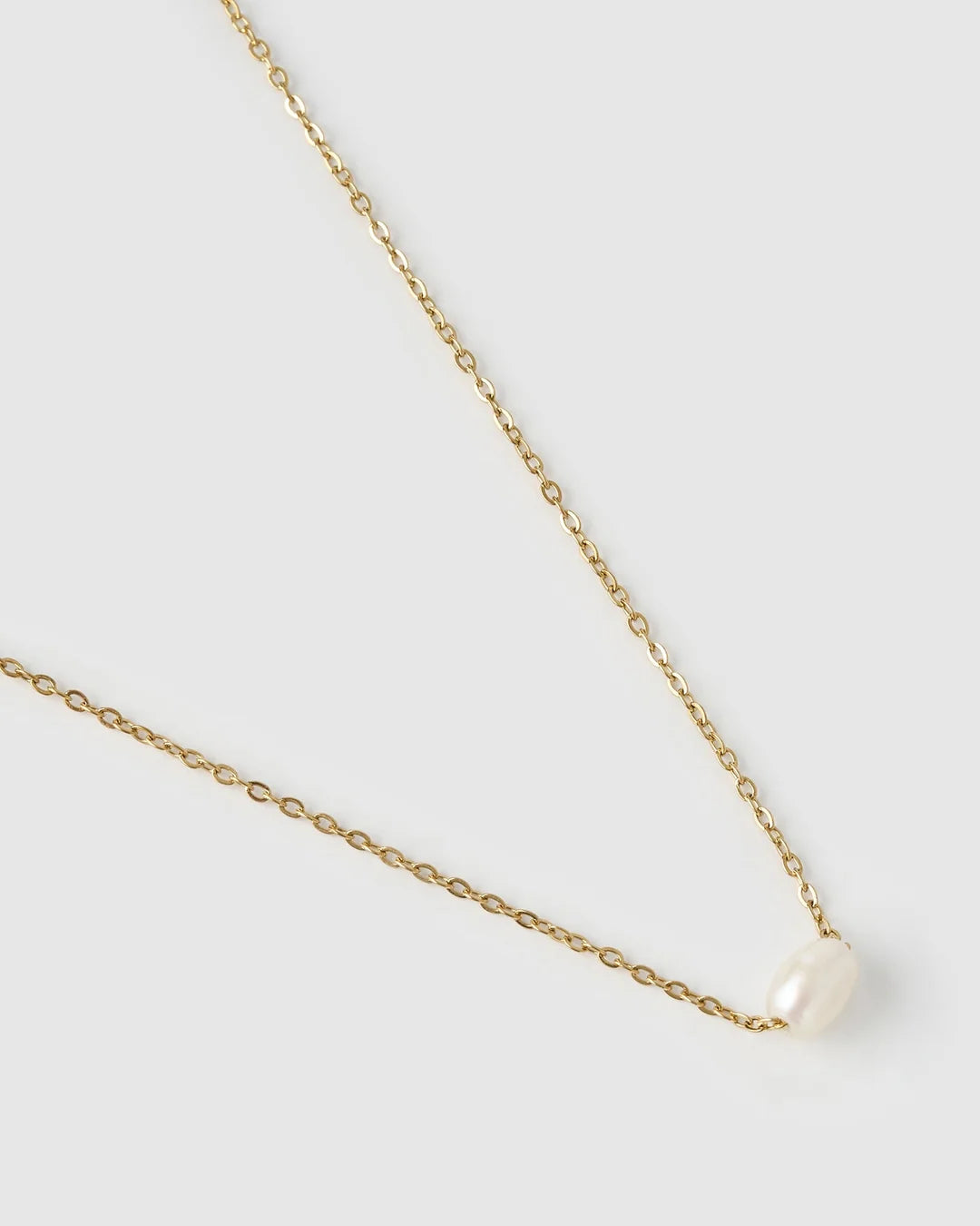 Gold necklace with a pearl pendant on a light gray background