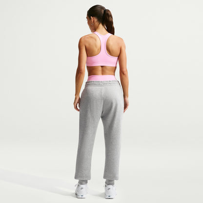 Woman wearing a pink sports bra and gray sweatpants on a light gray background