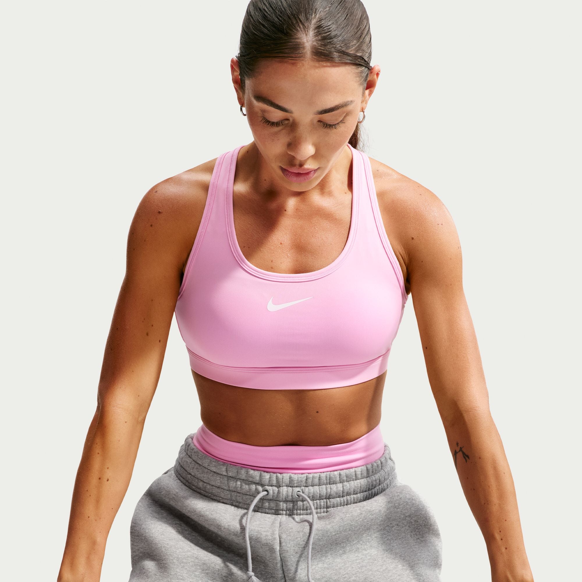 Woman wearing a pink Nike sports bra and gray sweatpants on a light gray background